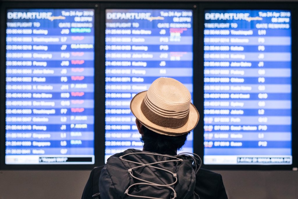 Traveler wearing a hat looking at a digital departure board at the airport