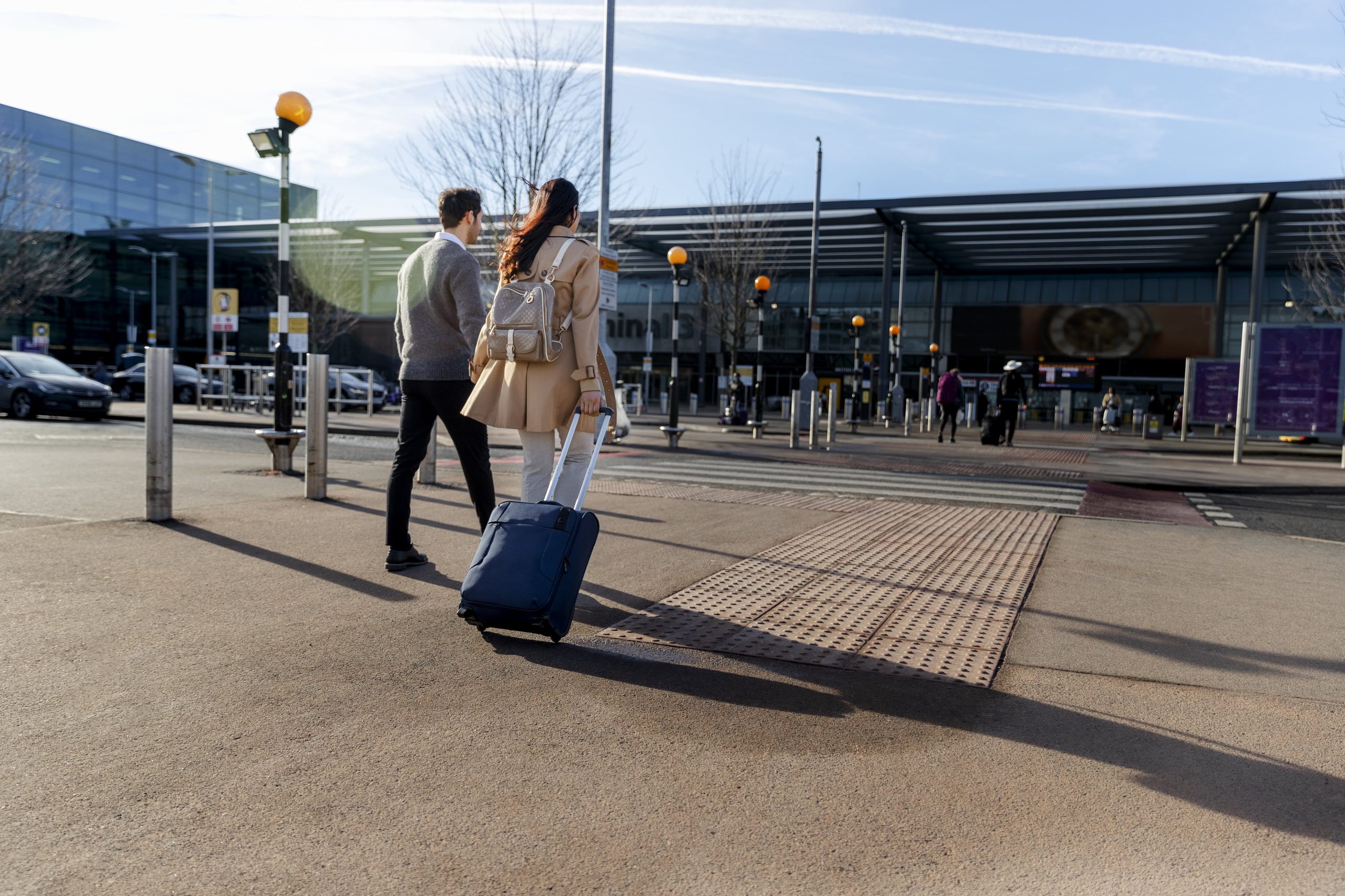 Travelers walking toward airport terminal with rolling luggage on a sunny day