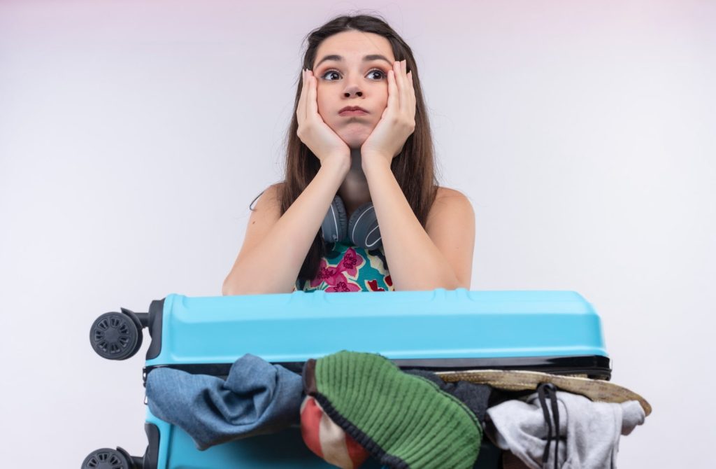 Traveler looking stressed behind an overpacked suitcase, illustrating concerns about how much is excess baggage at the airport.